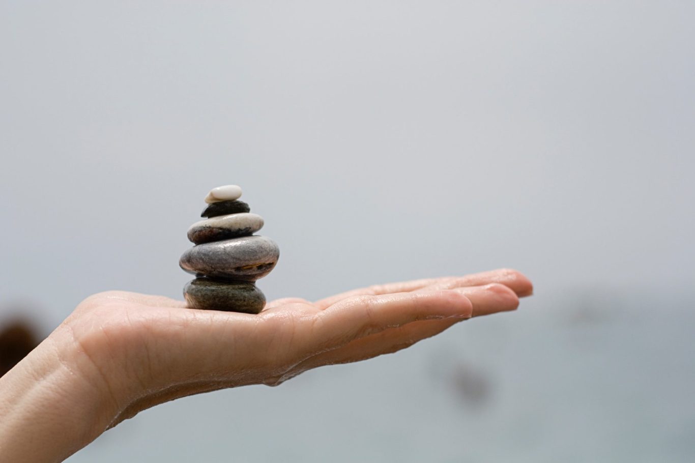 Eine Hand hält einen Stapel glatter Steine am Meer.